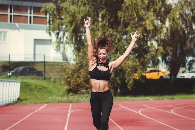 Opgewonden fit vrouwelijke hardloper in sportkleding en met koptelefoon met opgeheven armen tijdens het joggen gelukkig