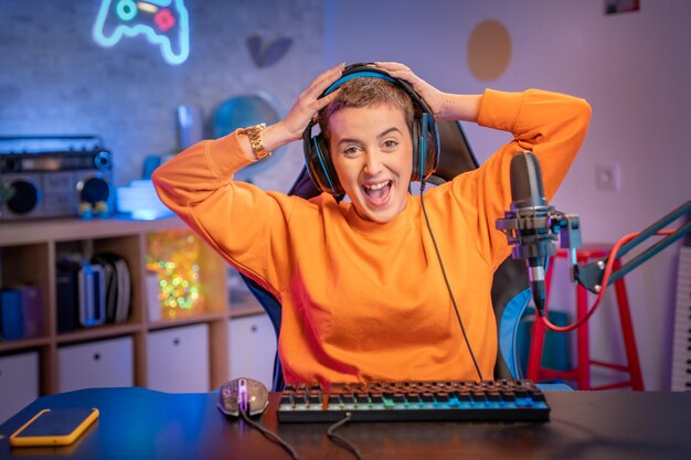 Opgewonden gamermeisje in headset met een microfoon die een online videogame speelt op haar pc