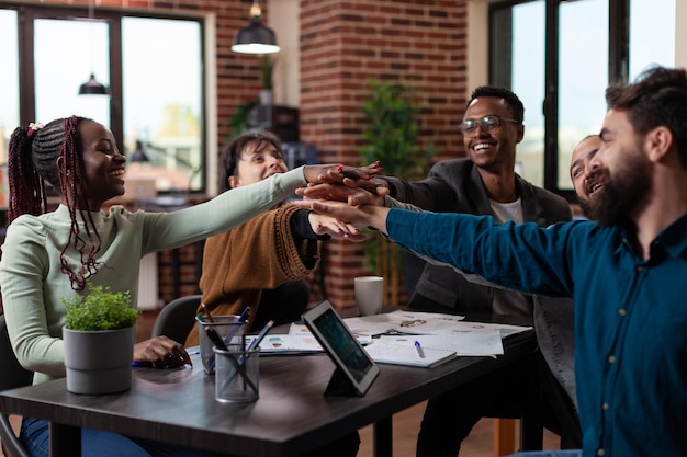 Opgewonden, gelukkig divers team dat lacht terwijl ze de bedrijfsprestaties viert tijdens een zakelijke bijeenkomst die in een startup-kantoor werkt. Multi-etnische zakenmensen die samen genieten