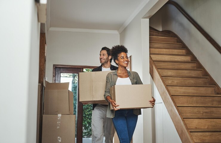 Foto opgewonden gelukkig en jong stel dat samen naar een nieuw huis verhuist terwijl ze huishoudelijke dozen dragen en inpakken glimlachende positieve en vrolijke man en vrouw in een mooi modern onroerend goed