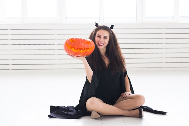 Opgewonden gelukkige jonge vrouw in halloween kostuum poseren met gesneden pompoen in lightroom.