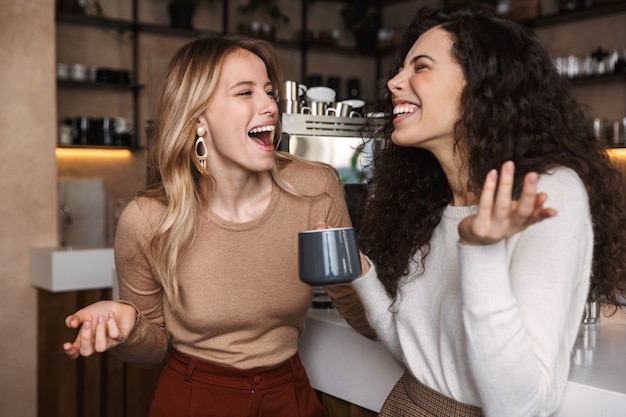 Opgewonden gelukkige mooie meisjesvrienden die in café koffie drinken