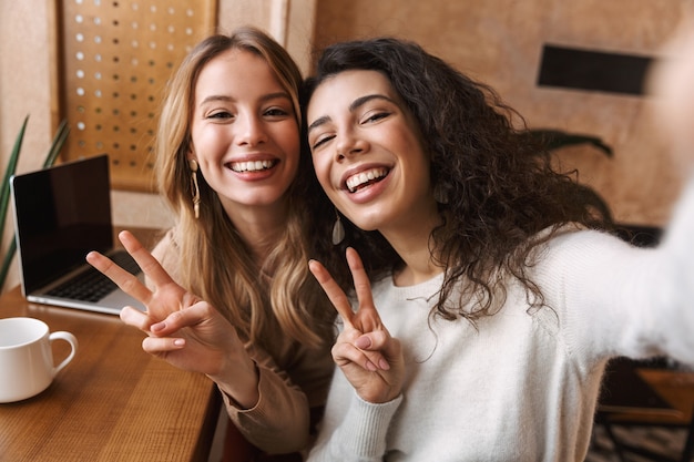 opgewonden gelukkige mooie meisjesvrienden die in café zitten, maken een selfie met de camera