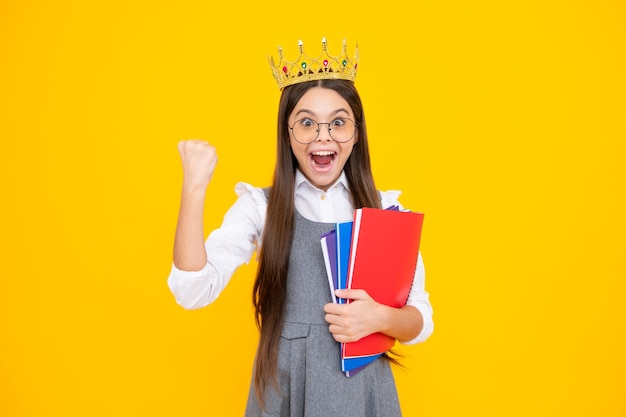 Opgewonden gezicht Schoolmeisje in schooluniform en kroon vieren overwinning op gele achtergrond School