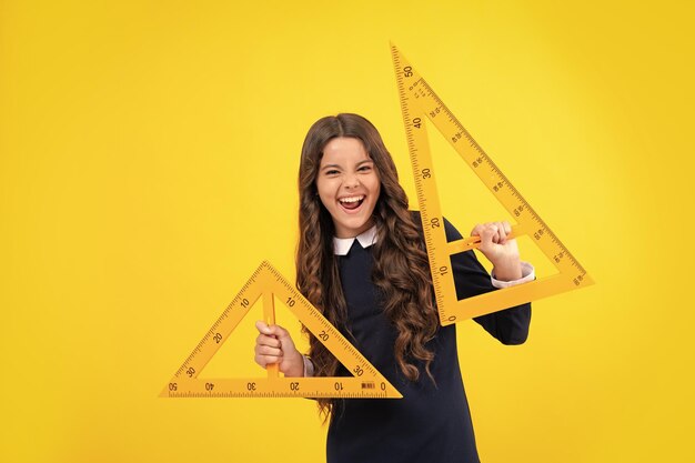 Opgewonden gezicht Terug naar school Schoolmeisje houdt liniaal meet geïsoleerd op gele achtergrond Verbaasde uitdrukking vrolijk en blij