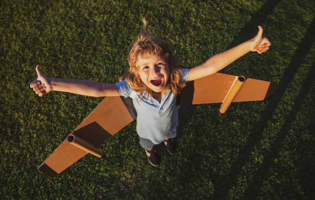 Opgewonden grappige kindjongen die in een vliegtuig vliegt gemaakt van kartonnen vleugels droom verbeelding jeugd bo