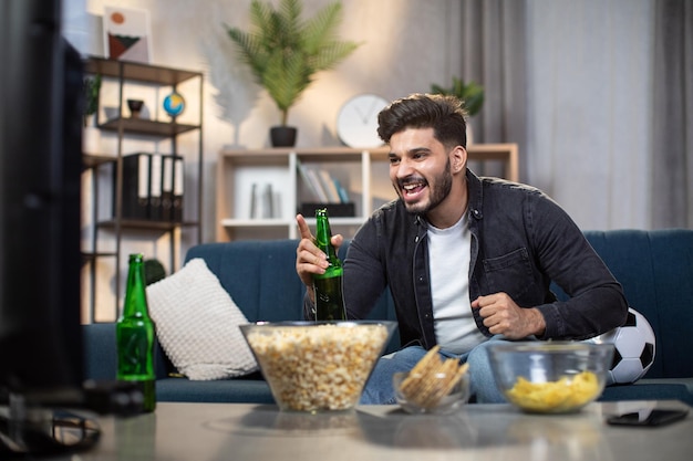 Opgewonden Indiase man met chips en bier voetbal kijken op tv