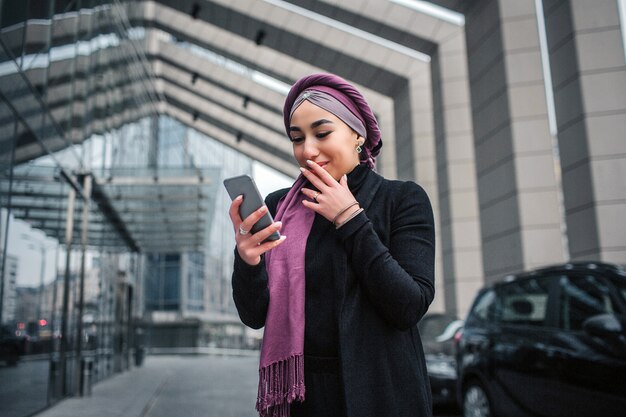 Opgewonden jonge Arabische vrouw staan buiten en kijk naar de telefoon.