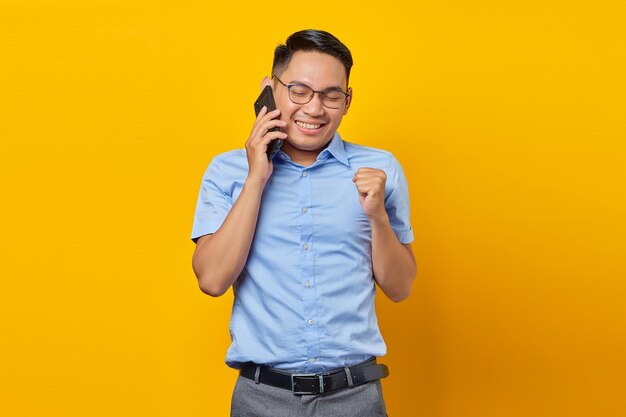 Opgewonden jonge Aziatische man Aziatische in glazen praten op mobiele telefoon geïsoleerd op gele achtergrond zakenman en ondernemer concept