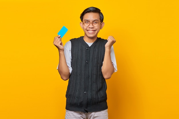Opgewonden jonge Aziatische man met creditcard geïsoleerd op gele achtergrond