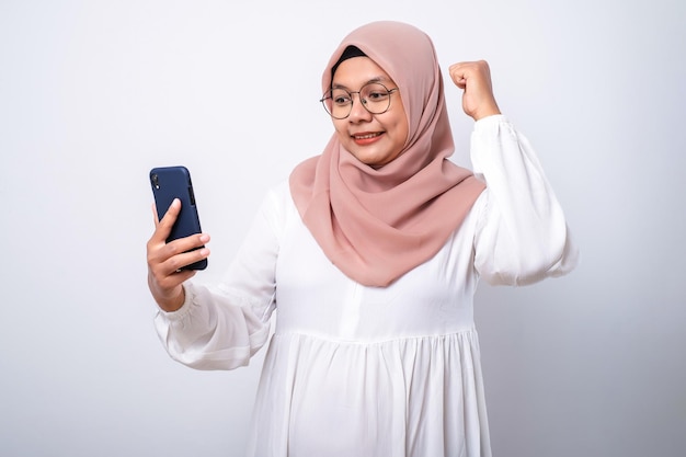 Opgewonden jonge Aziatische moslimvrouw die een mobiele telefoon gebruikt en succes viert met goed nieuws