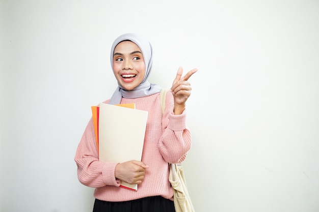 Opgewonden jonge Aziatische moslimvrouw student in roze trui met tas met boek