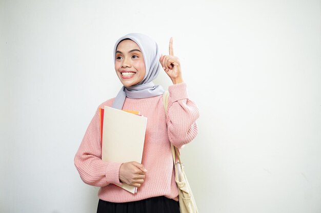 Opgewonden jonge Aziatische moslimvrouw student in roze trui met tas met boek