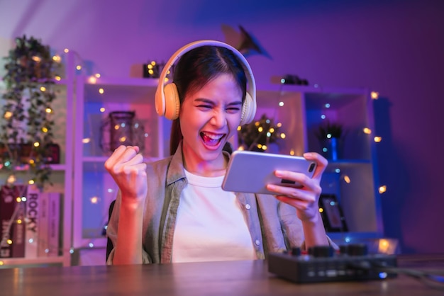Foto opgewonden jonge aziatische vrouw die een online spel speelt op een smartphone met gebalde vuisten om de overwinning te vieren die succes uitdrukt