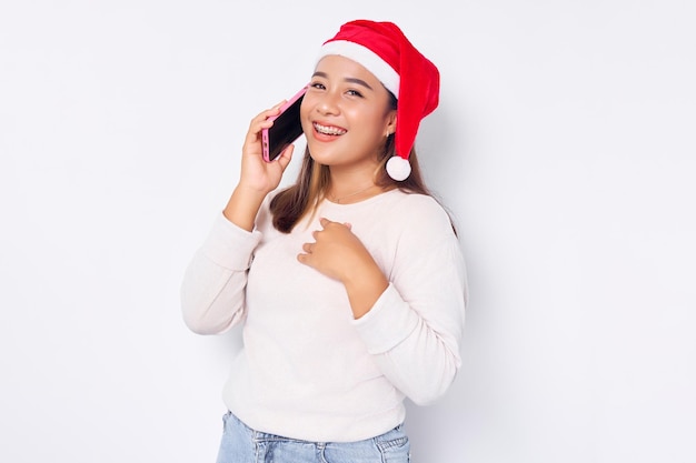 Opgewonden jonge Aziatische vrouw in een kerstmuts praten via de mobiele telefoon geïsoleerd op witte achtergrond viering Kerst vakantie en Nieuwjaar concept