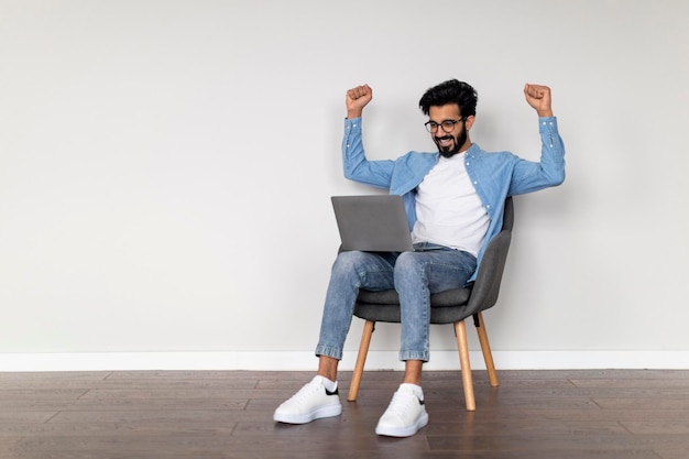 Opgewonden jonge Indiase man die laptop gebruikt en succes viert