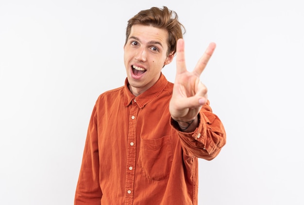 opgewonden jonge knappe kerel met een rood shirt met een vredesgebaar dat op een witte muur wordt geïsoleerd