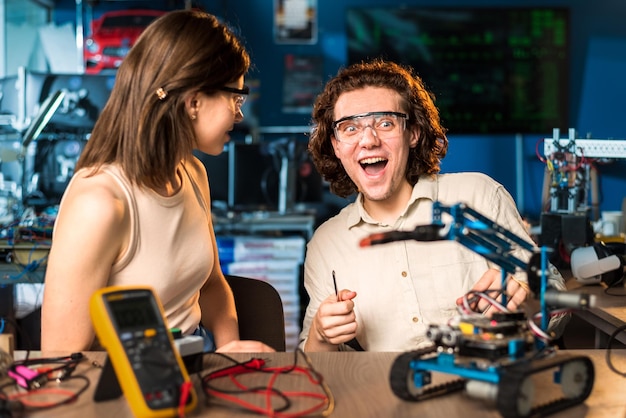 Opgewonden jonge man en vrouw in beschermende brillen die experimenten doen in robotica in een laboratorium