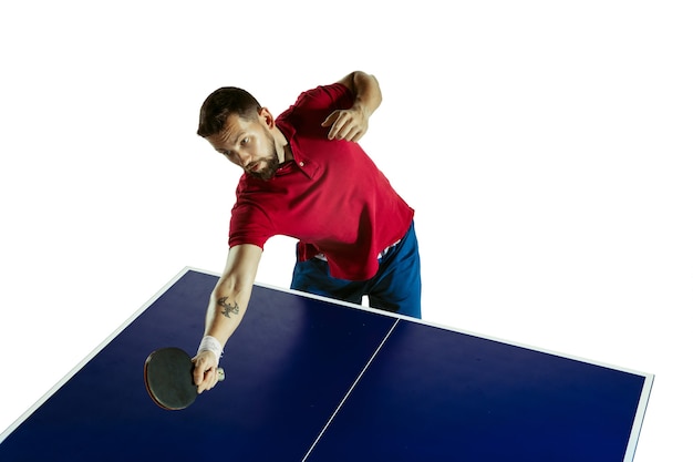 Opgewonden. Jonge man speelt tafeltennis op witte muur. Model speelt pingpong. Concept van vrijetijdsbesteding, sport, menselijke emoties in gameplay, gezonde levensstijl, beweging, actie, beweging.