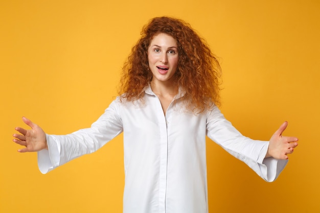 Opgewonden jonge roodharige vrouw meisje in wit overhemd poseren geïsoleerd op geel oranje muur