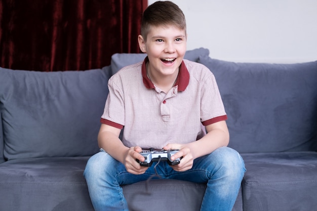 Opgewonden jonge tiener jongen gamer spelen van videogames met joystick zittend op de Bank thuis