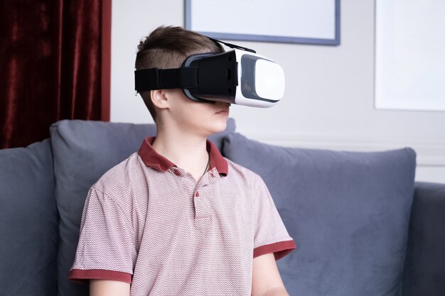 Opgewonden jonge tienerjongen in casual kleding met behulp van virtual reality-bril thuis.