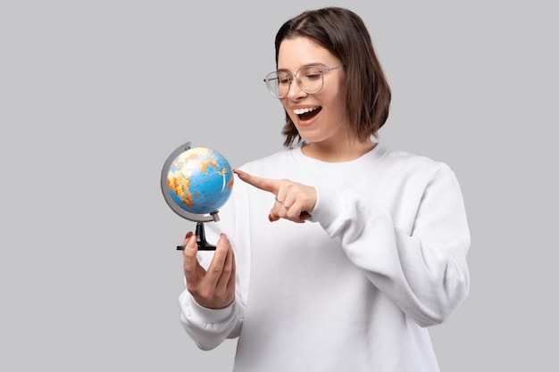 Opgewonden jonge vrouw wijst op een kleine earth globe studio shot