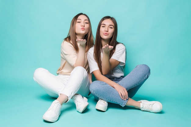 Opgewonden jonge vrouwen blazen kus poseren op de vloer geïsoleerd op turkooizen muur.