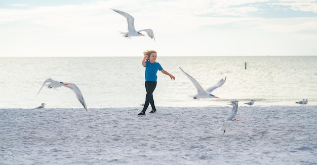 Opgewonden jongen die op het strand rent kind en zeemeeuw op het strand verbaasde jongen die met de zijne op het strand rent