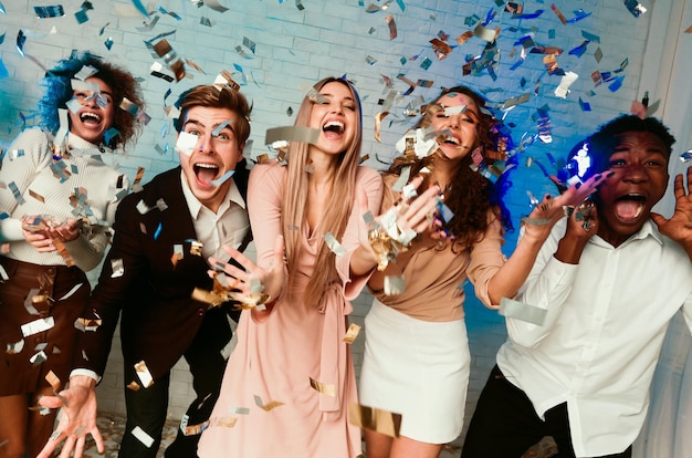 Opgewonden jongeren staan onder een stort van glanzende confetti en vieren binnen