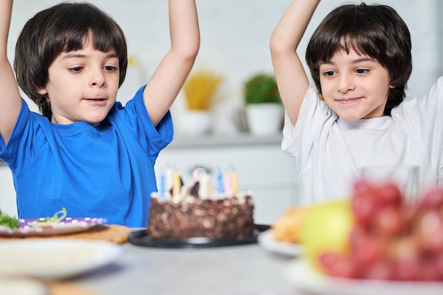 Opgewonden kleine spaanse tweeling die er gelukkig uitziet na het blazen van kaarsen op een verjaardagstaart. kinderen vieren verjaardag samen met ouders thuis. selectieve focus op kinderen