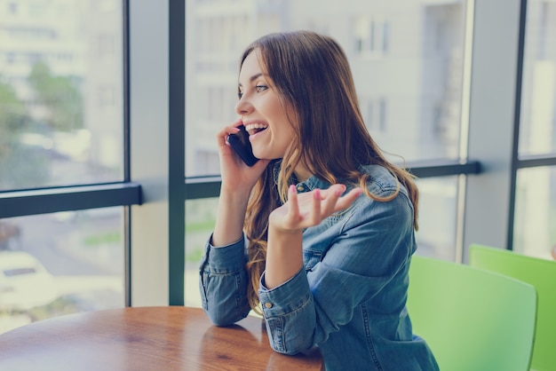 Opgewonden lachen mooie vrouw zittend in een café, ze praat aan de telefoon en roddelen met haar beste vriend