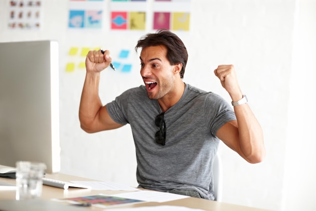 Opgewonden man en computer met viering in het kantoor voor daghandel bonus en investering groei Gelukkige investeerder en creatieve persoon met vuist in het winnen voor de beurs winst of nieuws van succes