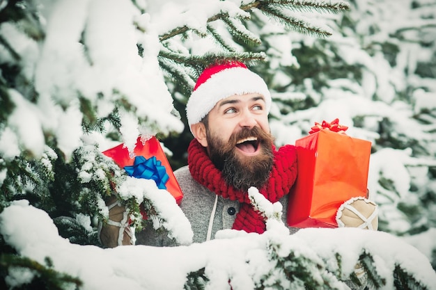 Opgewonden man houdt de huidige doos vast met een bebaarde man in de kerstmuts in het besneeuwde winterbos