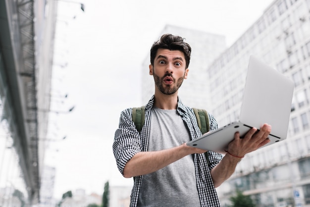 Opgewonden man met laptop, online winkelen, staande op de straat van de stad