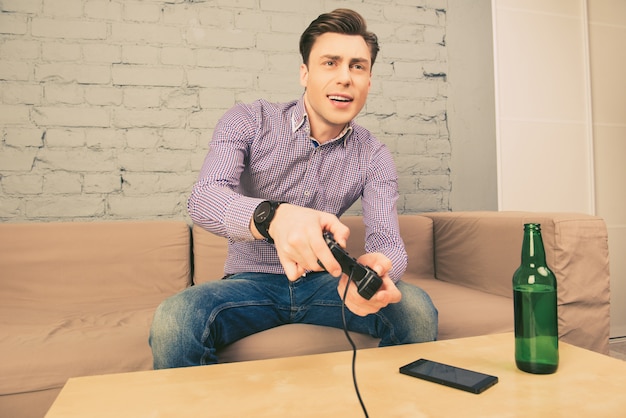 Opgewonden man zittend op de Bank met flesje bier en spelen van videogames