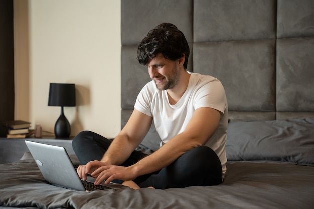 Opgewonden man zittend op een bed met een laptop viert succes