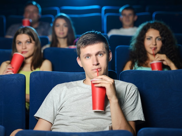 Opgewonden mannen kijken naar film in de bioscoop en drinken frisdrank