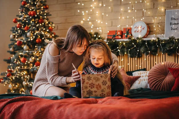 Opgewonden meisje met moeder opent geschenkdoos van de kerstman, gelukkige jeugd, vakantieviering, kerstwonder