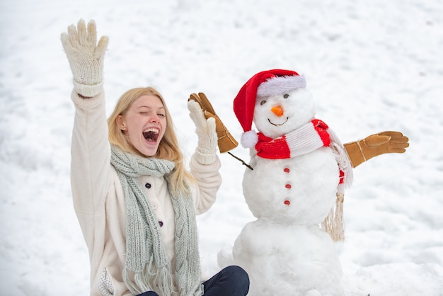 Opgewonden meisje plaing met een sneeuwpop op een besneeuwde winterwandeling. Sneeuwpop en winterplezier maken. Schattig