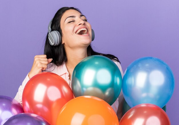 Opgewonden met gesloten ogen jong mooi meisje met een koptelefoon achter ballonnen