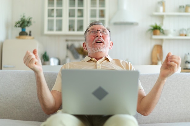 Opgewonden middeljarige oudere man euforische winnaar oudere volwassen grootvader kijkt naar laptop lezen