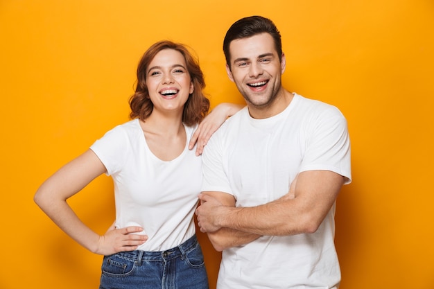 Opgewonden mooi paar dat witte t-shirts draagt die geïsoleerd over gele muur staan