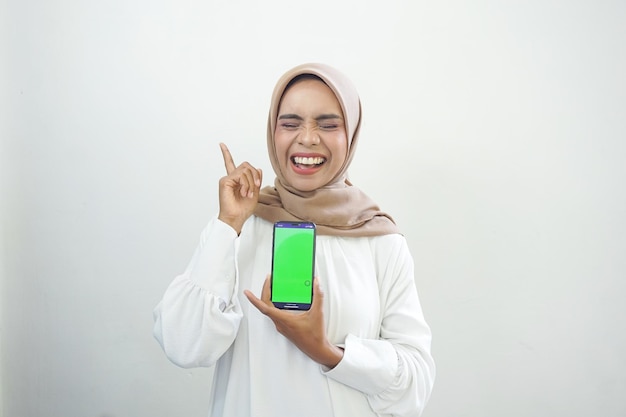 Opgewonden mooie Aziatische moslimvrouw met groen scherm mobiele telefoon geïsoleerd op wit
