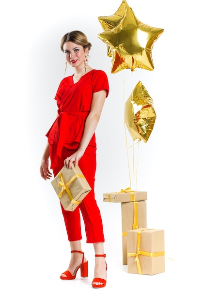 Opgewonden mooie blonde dame in rood kostuum met stapel geschenkdozen over witte studio achtergrond. Vrouwendag, Valentijnsdag, verjaardag, jubileum vieren. Winkelen voor vakantieconcept