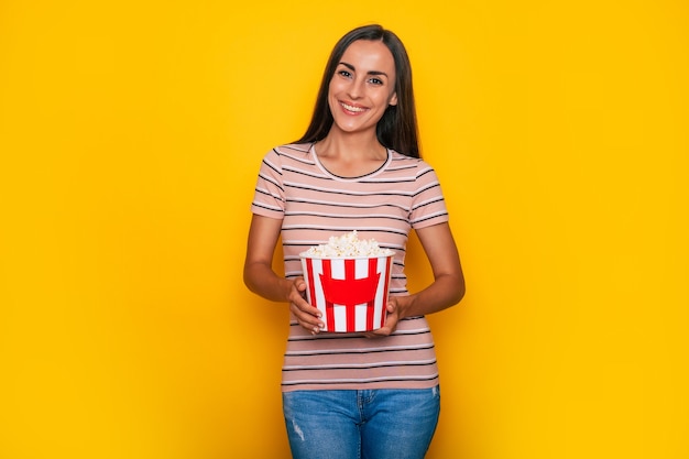 Opgewonden mooie moderne jonge brunette vrouw in vrijetijdskleding en 3D-bioscoopbril en grote mand popcorn poseert tijdens het kijken naar een film in de bioscoop