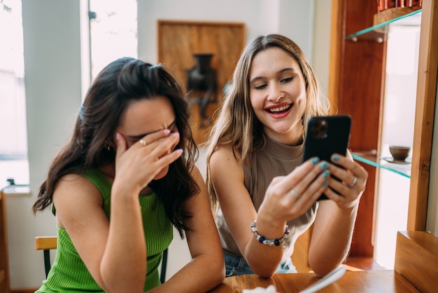 Opgewonden mooie twee Latijnse vrouwen kijken grappige video op moderne mobiele telefoon