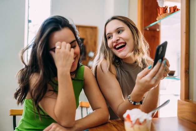 Opgewonden mooie twee Latijnse vrouwen kijken grappige video op moderne mobiele telefoon