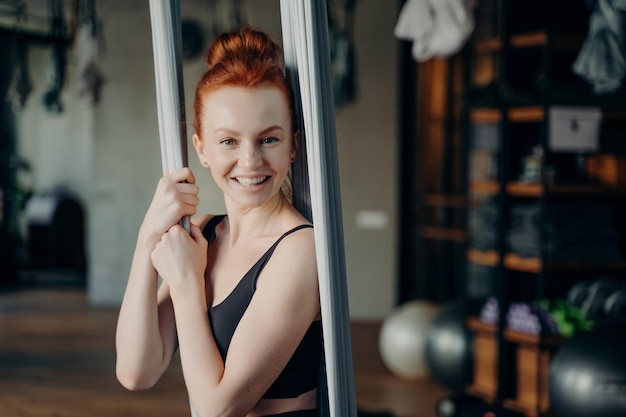 Opgewonden roodharige vrouw genieten van luchtyoga in fitnessstudio