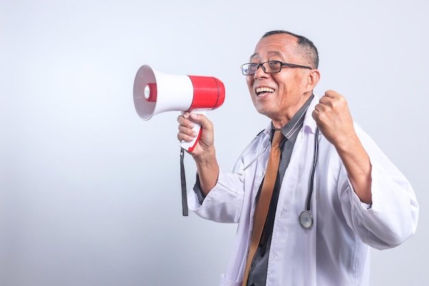Opgewonden senior Aziatische arts die de vuist knelt en een megafoon vasthoudt, kondigt goed medisch nieuws aan
